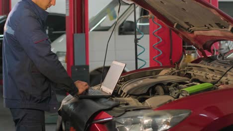 computer diagnostics of cars, young mechanic specialist male uses laptop technology while repairing vehicle with open hood at service station