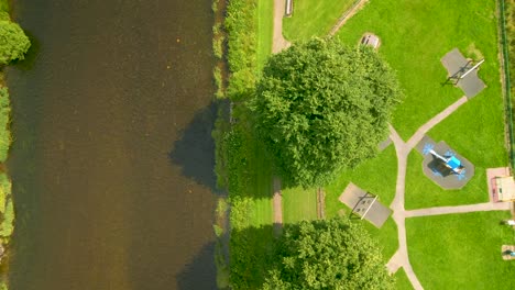 Luftdrohnenaufnahme-Beim-Überfliegen-Eines-Flusses-Neben-Einem-Park-Mit-Bäumen