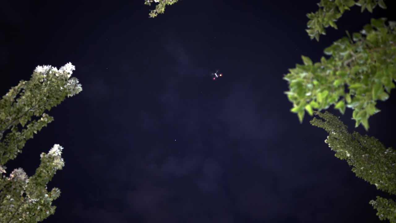 나무 옆 밤하늘을 나는 드론, 지상에서 보기