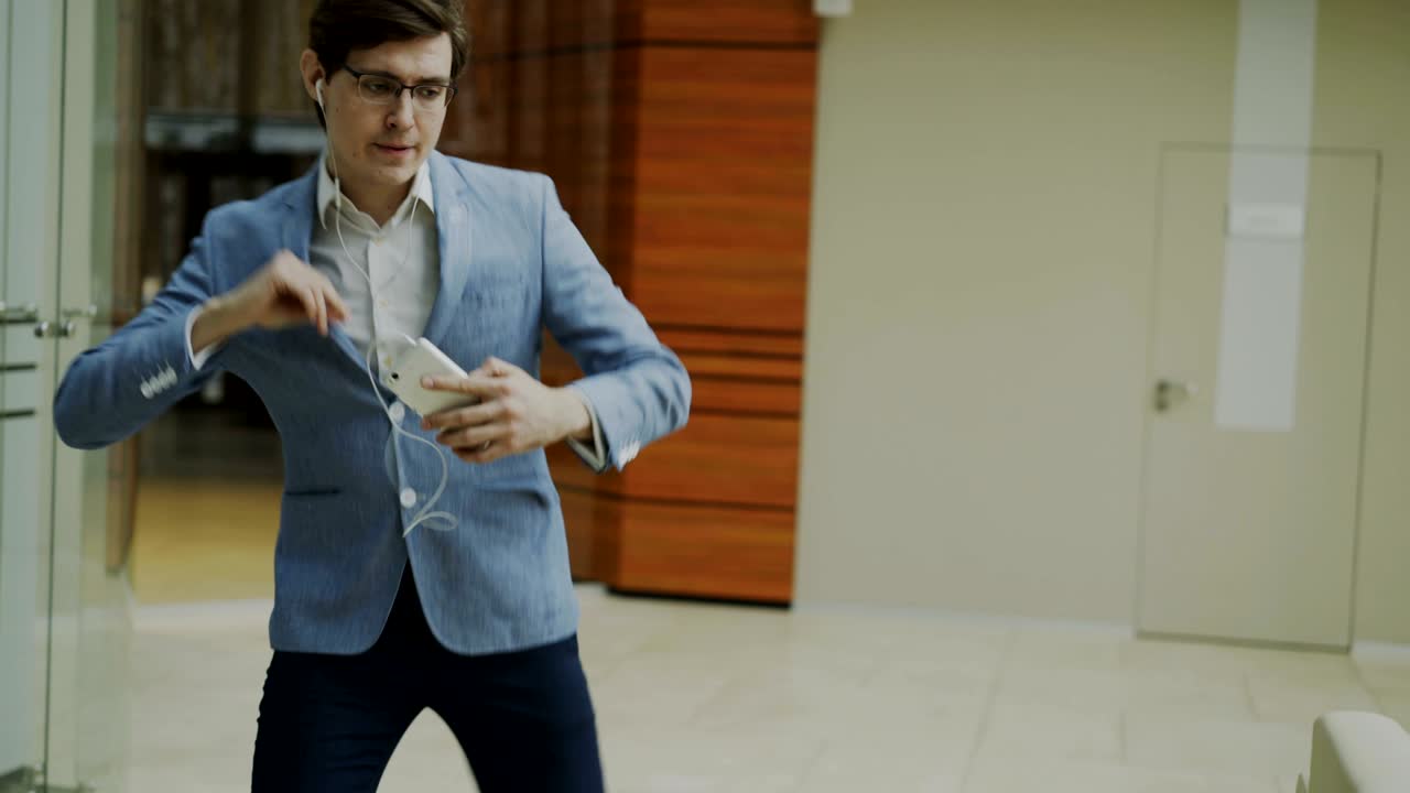 hombre de negocios feliz escuchando música con auriculares bailando y caminando en el vestíbulo de una oficina moderna