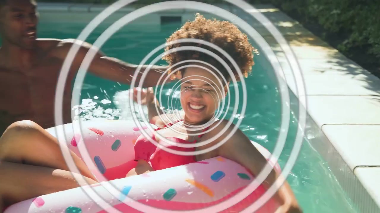 Woman lying on pink donut, man coming and splashing, man tossing ball, playing, rings overlay ads
