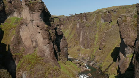 Drone-flying-through-deep-Fjadrargljufur-canyon-in-south-Iceland.-Amazing-rock-formation,-erosion-of-Fjadra-river,-geological-landscape.-Tourist-on-viewpoint-watching-stunning-icelandic-panorama