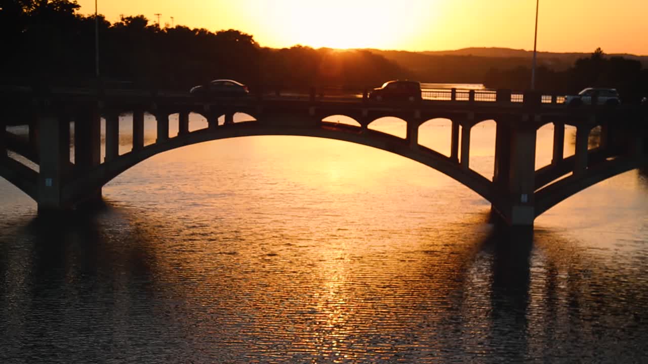 Peering through railing at cars driving on bridge over river during rush hour at sunset