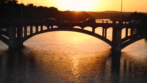 peering through railing at cars driving on bridge over river during rush hour at sunset