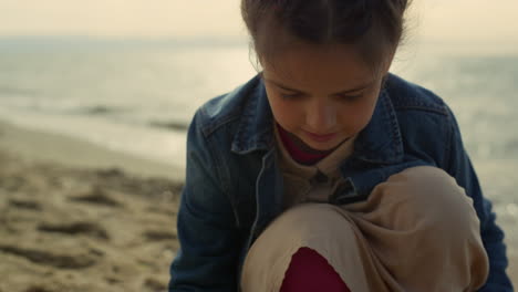 little girl drawing sand on sea beach. cute kid playing game on ocean coast.