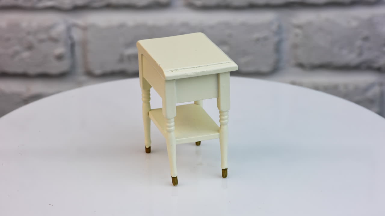 Toy wooden piece of furniture in studio. Tiny white nightstand with a cute drawer and shiny golden knob. Toy furniture circling isolated against wall background.