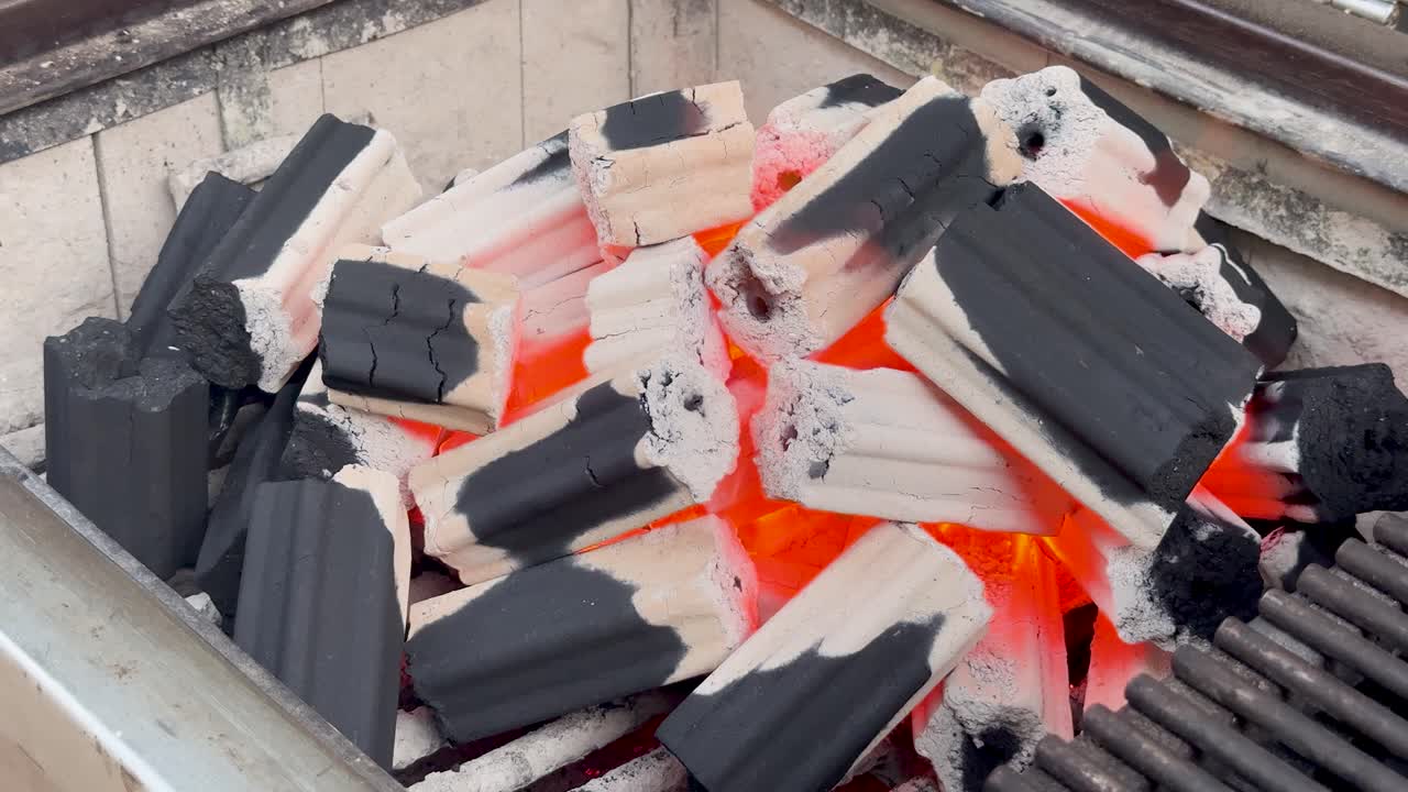 Primer plano de briquetas de carbón ardiendo con calor intenso y brasas rojas incandescentes dentro de una parrilla