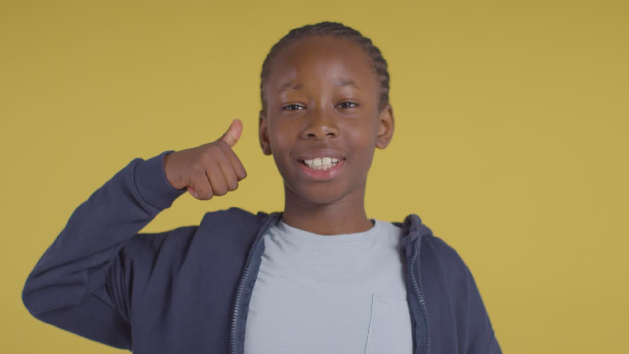 retrato de estudio de un niño sonriendo y dando un gesto con el pulgar hacia arriba contra el fondo amarillo 1