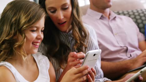 madre e hija usando teléfono móvil en la sala de estar