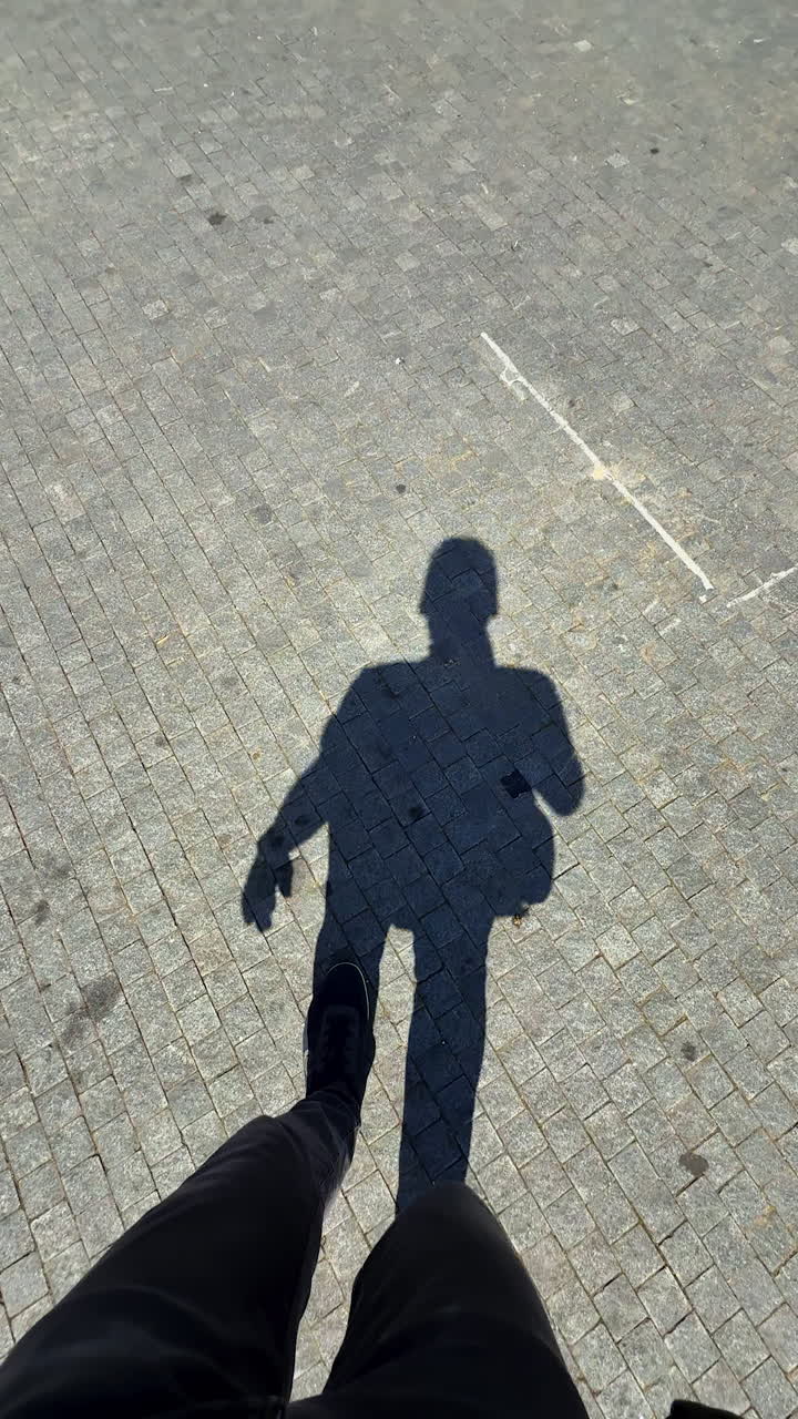 Daytime shadow on pavement. A person walks on a sunlit paved area, creating a clear shadow. The scene captures the movement and sunlight