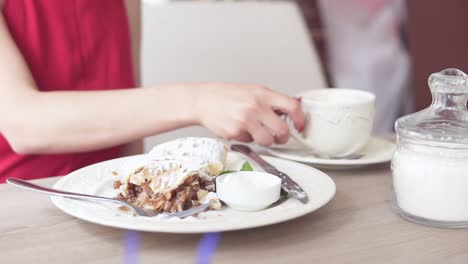 unrecognizable girl in red dress drinking coffee and taking desert strudel at the restaurant using fork and knife. beautiful