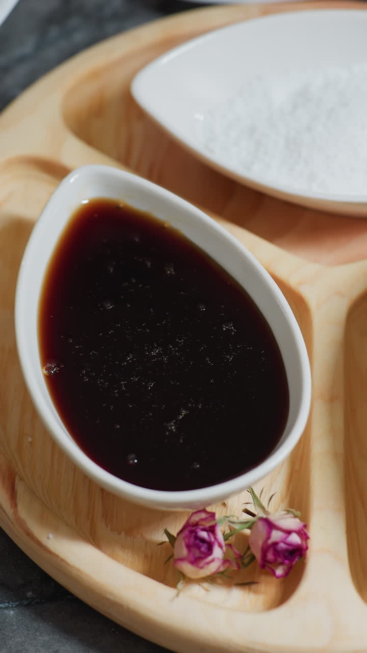 목판 위에 향신료, 설탕 및 소스와 함께 세라 그에 있는 커피의 클로즈업, 작은 분홍색 꽃이 장식적인 터치를 추가하고, 베이킹 재료와 쿠키 커터가 배경에 배열되어 있습니다.