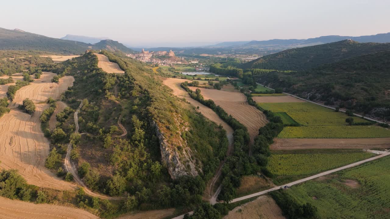 Orbital drone shot of a Spanish countryside showing a distant village, rolling hills, and farmlands in Valderama, Spain.