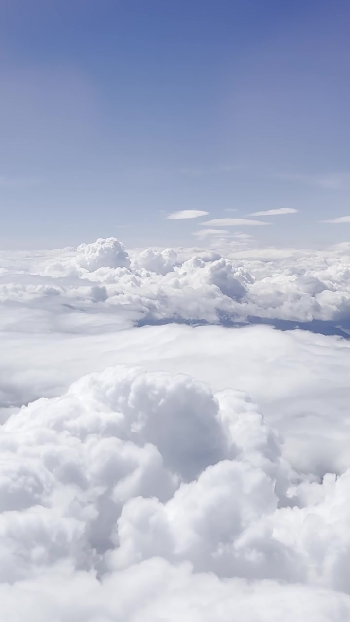 Puncak awan putih menjulang tinggi memenuhi cakrawala di bawah langit biru cerah selama penerbangan pesawat, latar belakang vertikal