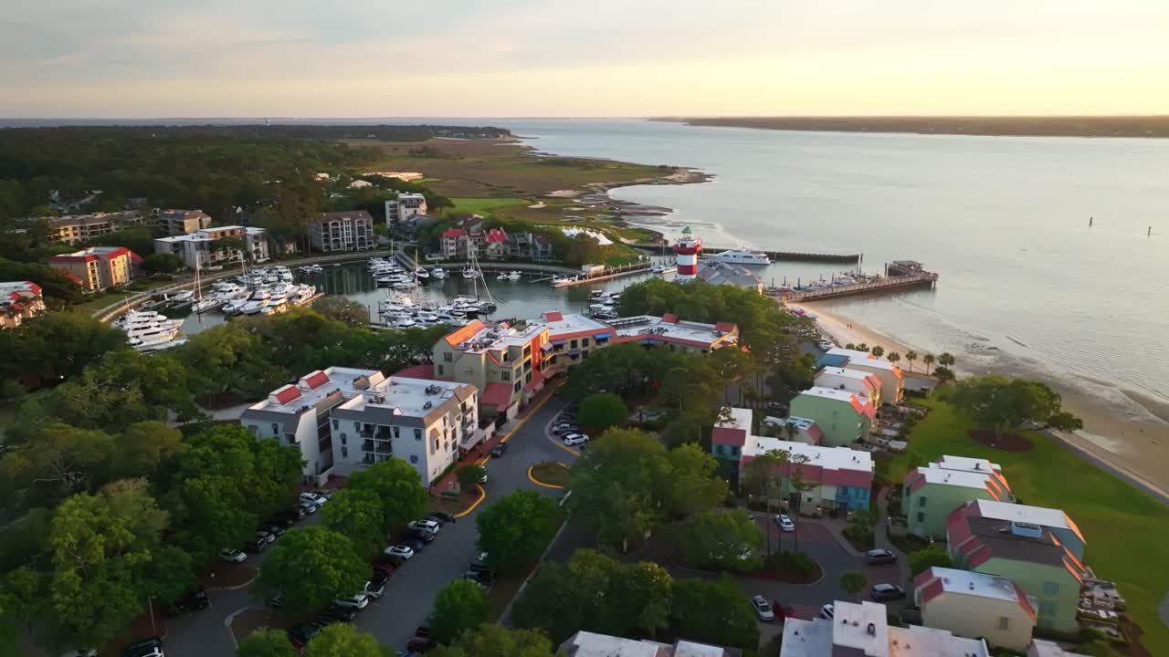 Drone pullback across harbor town skyline under sunset, boats moored along coastal piers, Harbour Town Pier South Carolina USA