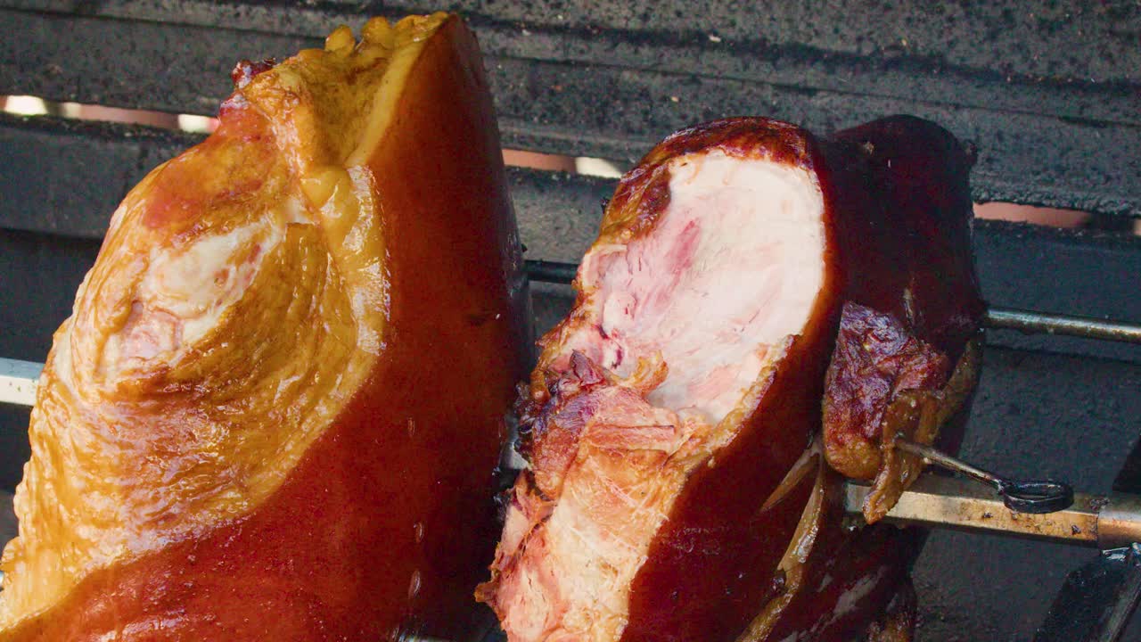 Juicy pork knuckle rotates on spit above open wood fire, golden-brown skin, outdoor market