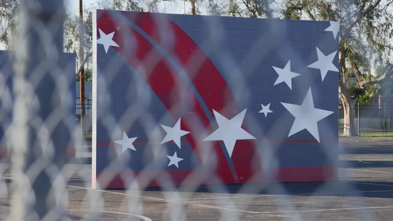 Tilt up and rack focus into an empty school playground on a sunny day through a chainlink fence.