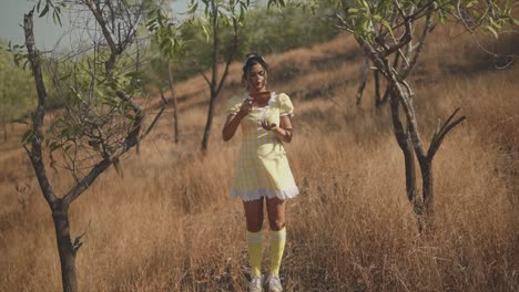 pretty woman in a yellow dress standing in the middle of the grass picking olives with a clay jug on a beautiful sunny day