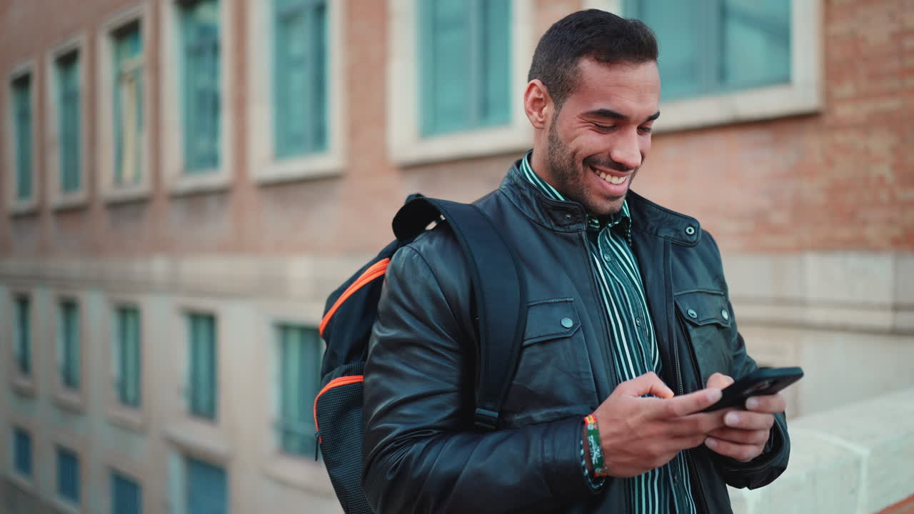 Giovane uomo che scrive messaggi sullo smartphone e sorride all'aperto.