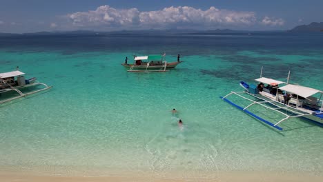 4K-drone-video-of-a-couple-running-into-the-crystal-clear-blue-waters-on-Banal-Beach-while-on-a-boat-tour-from-Coron-in-Palawan,-Philippines