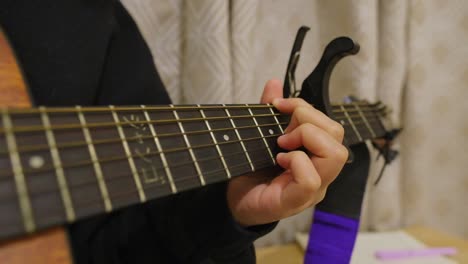 caucasian person strumming acoustic guitar with capo attached