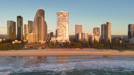 aerial view of gold coast's skyline at sunrise, highlighting skyscrapers and ocean waves in warm golden light