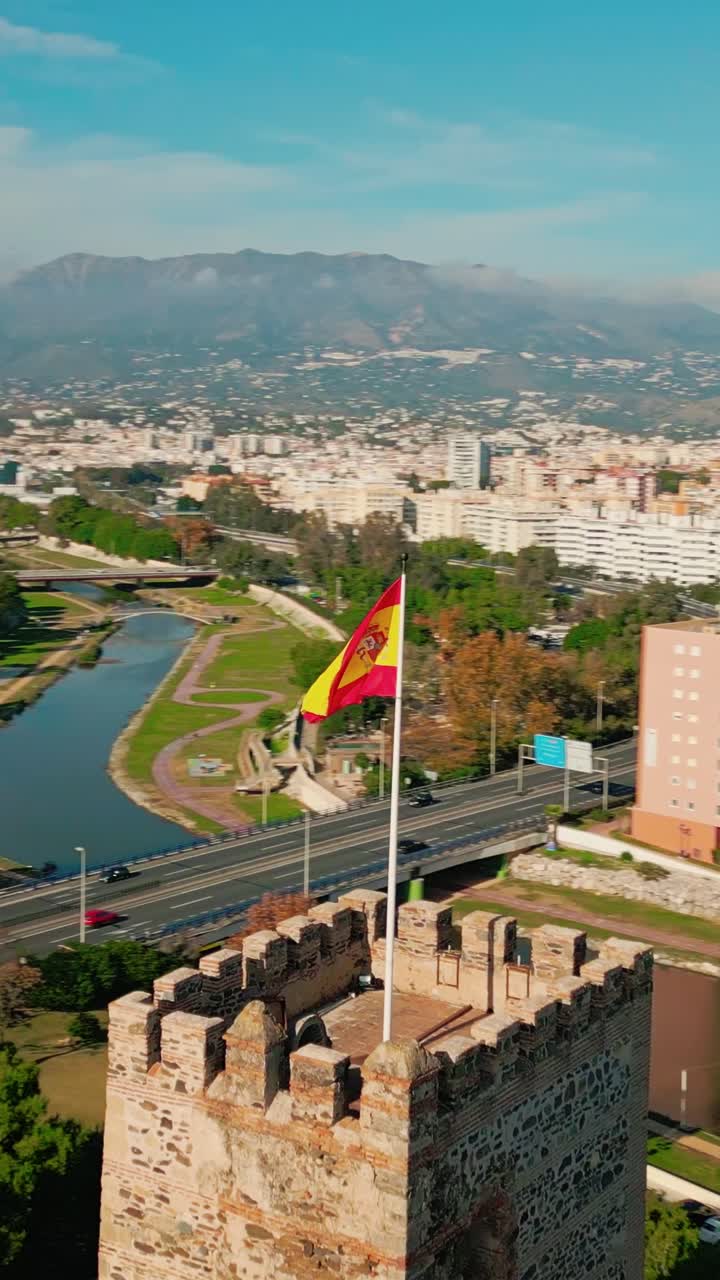 Lodret luftoptagelse af spansk flag, der vajer over den historiske fæstning Sohail Castle i Fuengirola, Andalusien, Costa del Sol, Spanien, smuk solrig middelhavskystudsigt