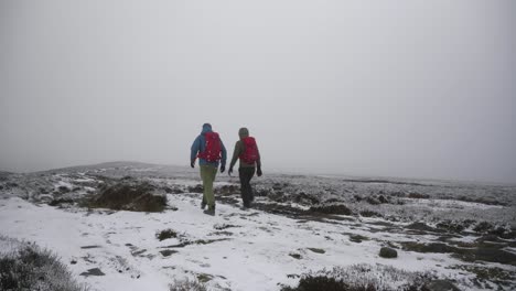 Two-people-hiking-through-open,-cloudy,-frozen,-winter-tundra