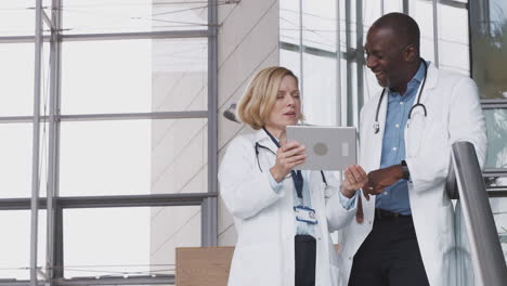 male and female doctors having informal meeting in modern hospital looking at digital tablet