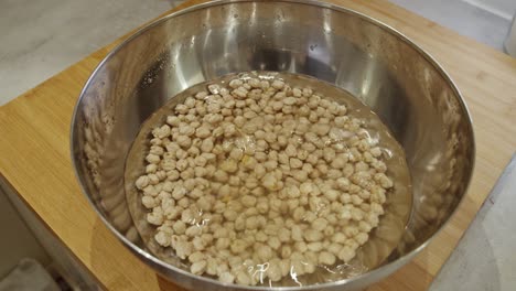 chef puts a metal bowl with chickpeas for soaking on a wooden table in the kitchen