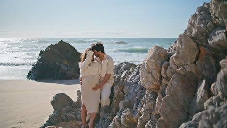 una pareja embarazada amorosa posando apoyándose en los acantilados de la playa en un día de verano. embarazo en pareja