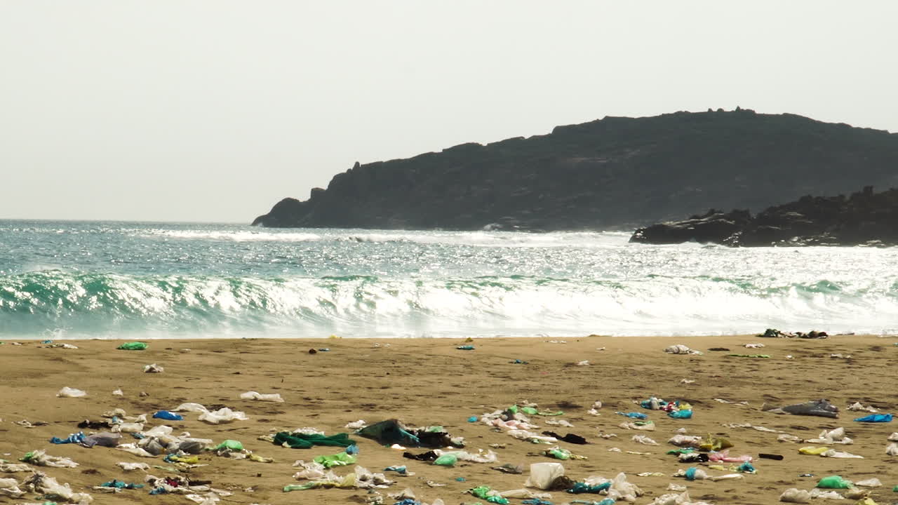 las olas del océano se estrellan contra la basura plástica sucia y contaminada, los desechos de la playa de arena, se alejan del lugar natural de la basura de los vertederos en la costa del paisaje marino