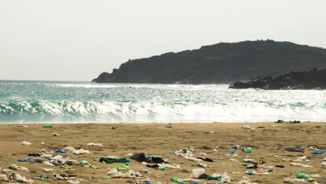 ocean waves crashing in to dirty polluted plastic trash waste sandy beach, zoom out on landfill garbage natural spot on seascape coastline