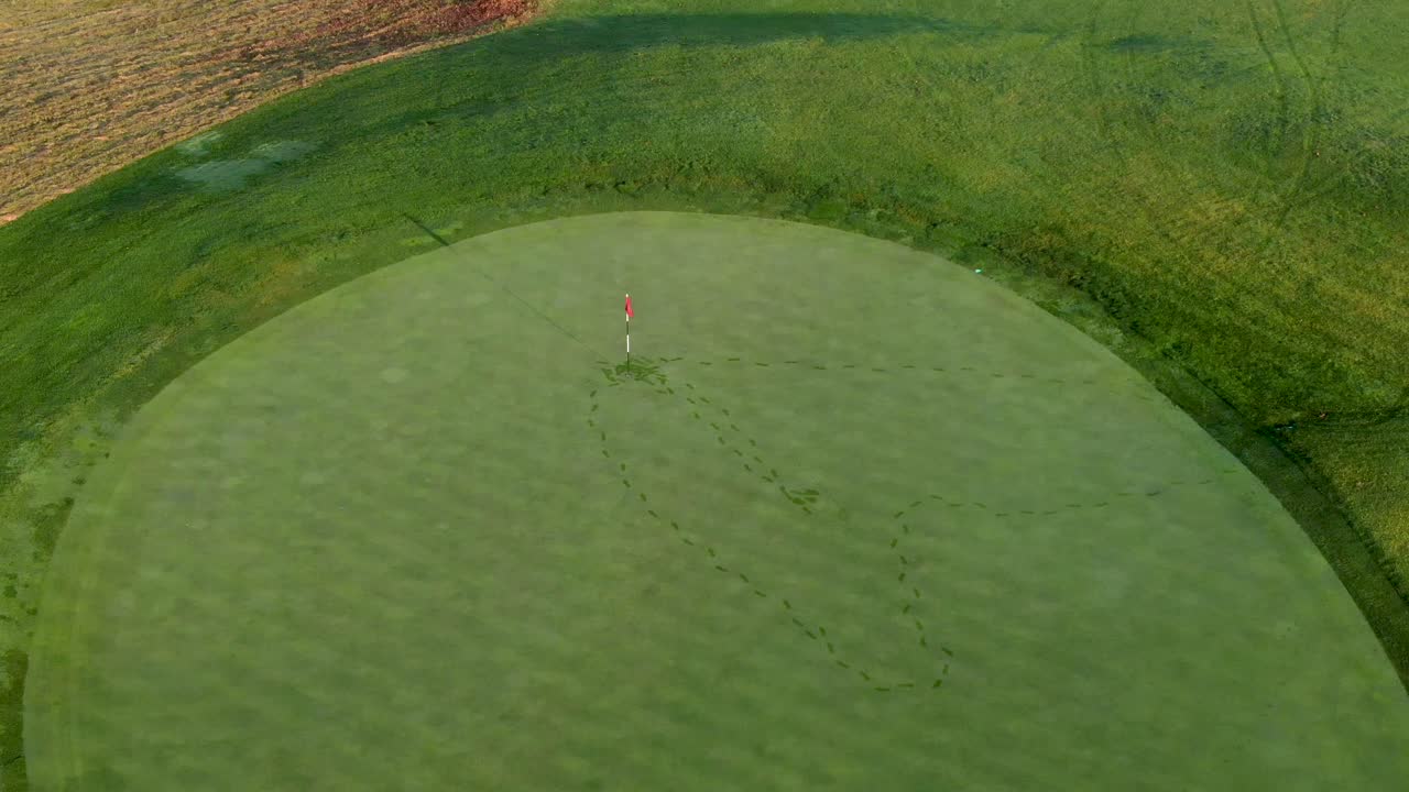 페어웨이의 깃발 위로 공중 기울기, 아침 이슬 서리에 잔디에 발자국이 보입니다.