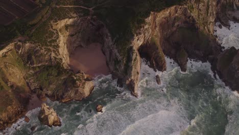 Top-down-of-small-beach-with-high-cliffs-at-Portugal,-aerial