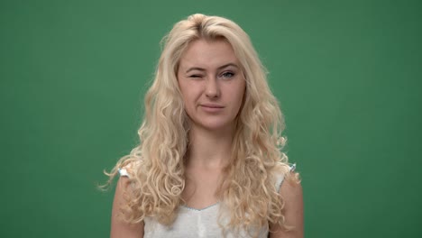 young blonde woman in a white top is  winking and smiling, chroma key green screen background