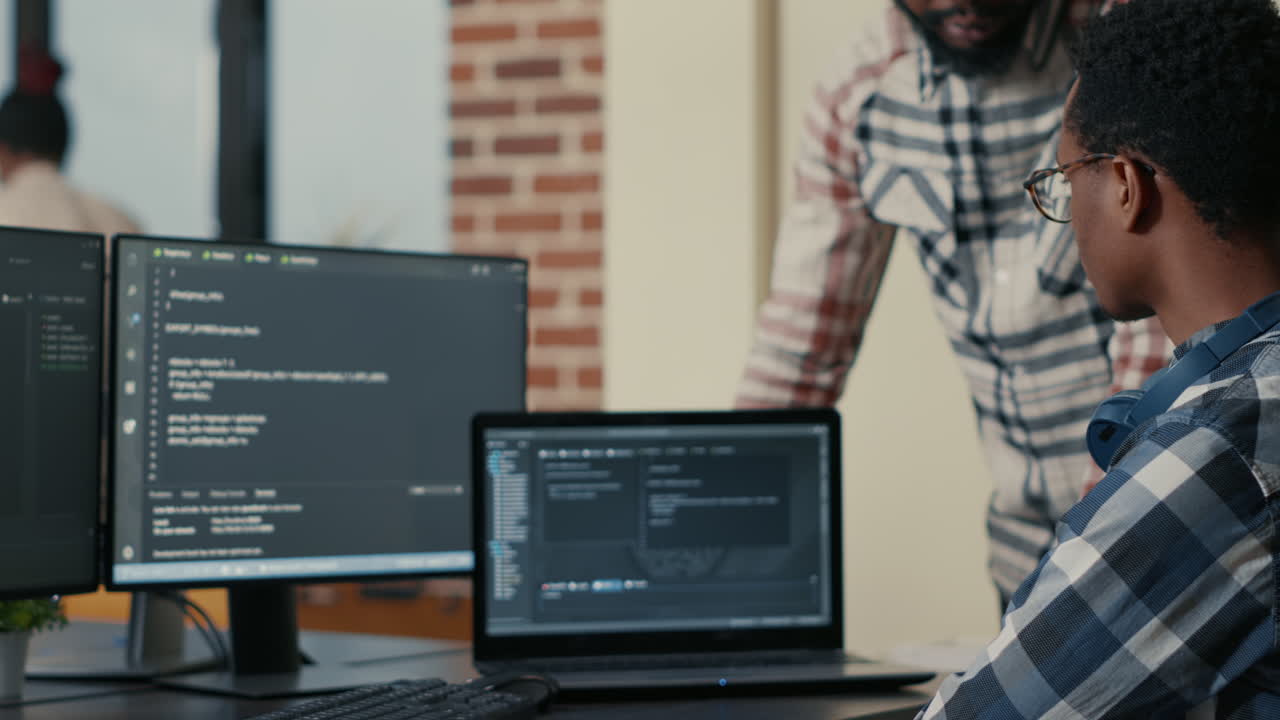Focused software developer writing code on laptop looking at multiple screens with programming language