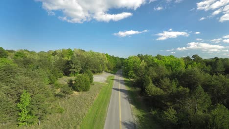 aerial view with a slow push in down beautiful lush country road in the summer. forest, trees, and nature all visible in this cinematic shot