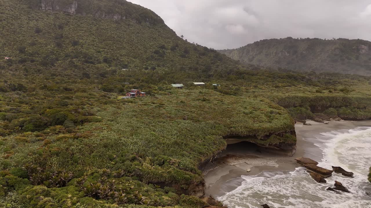 Costa selvaggia e remota con grotta marina e lussureggiante foresta pluviale in una giornata nuvolosa sulla costa occidentale della Nuova Zelanda. Ripresa aerea con drone.