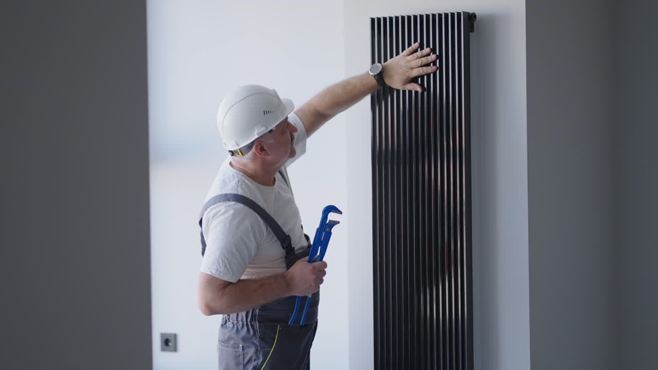 Plumber checks the operation of the batteries after the start of the boiler room in the house before the heating season