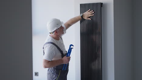 plumber checks the operation of the batteries after the start of the boiler room in the house before the heating season