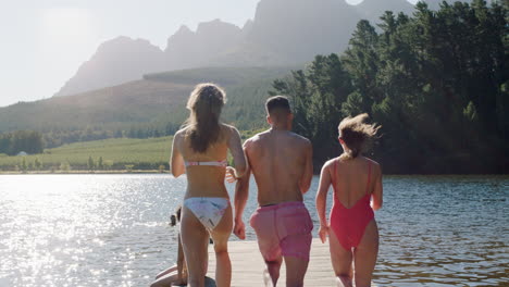 Grupo-De-Amigos-Corriendo-Saltando-Del-Embarcadero-En-El-Lago-Al-Atardecer-Divirtiéndose-Chapoteando-En-El-Agua-Disfrutando-De-La-Libertad-Compartiendo-Aventuras-De-Verano