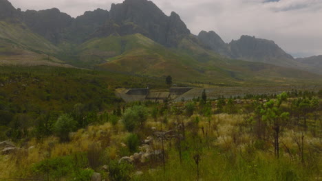 Vorwärts-Fliegen-über-Wilde-Grüne-Vegetation-In-Der-Landschaft.-Aufschlussreicher-Staudamm-Unter-Hohem-Bergrücken-Im-Hintergrund.-Südafrika