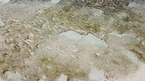 Aerial-drone-birds-eye-view-of-ocean-and-sand-patterns-with-coral-reef-during-low-tide-in-Timor-Leste,-Southeast-Asia