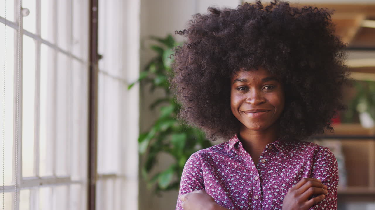 Giovane creativa afroamericana millennial in piedi in un ufficio che si gira e sorride alla telecamera, primo piano