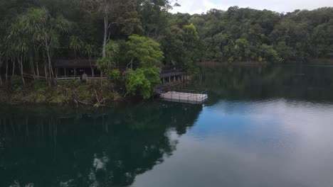 Aerial-video-showing-a-popular-holiday-area-on-a-volcanic-crater-lake-with-a-pontoon-floating-by-the-shore