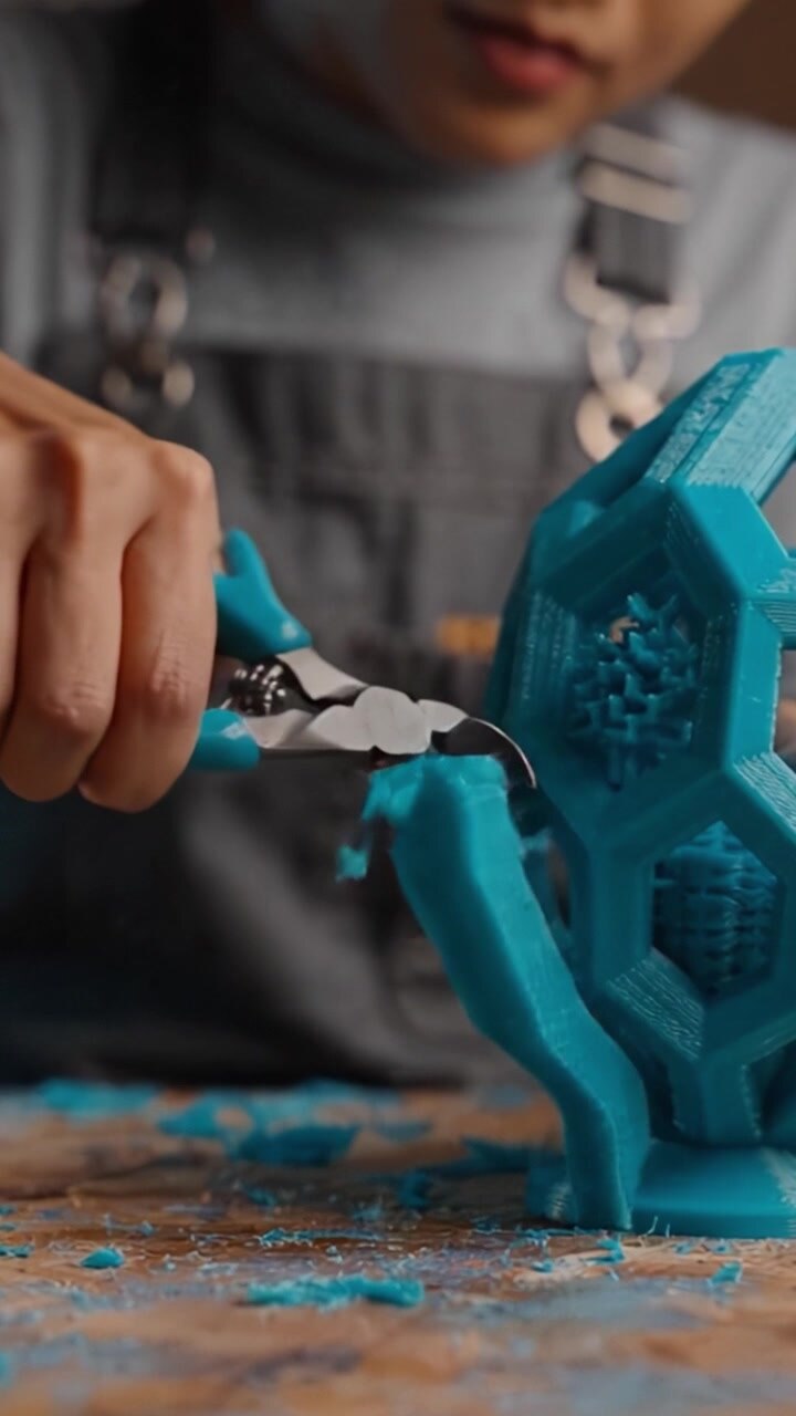 A Craftsperson Carefully Trims a 3D Printed Blue Object with Precision Tools, Highlighting the Intricacies of 3D Printing and the Art of Creating Functional Designs
