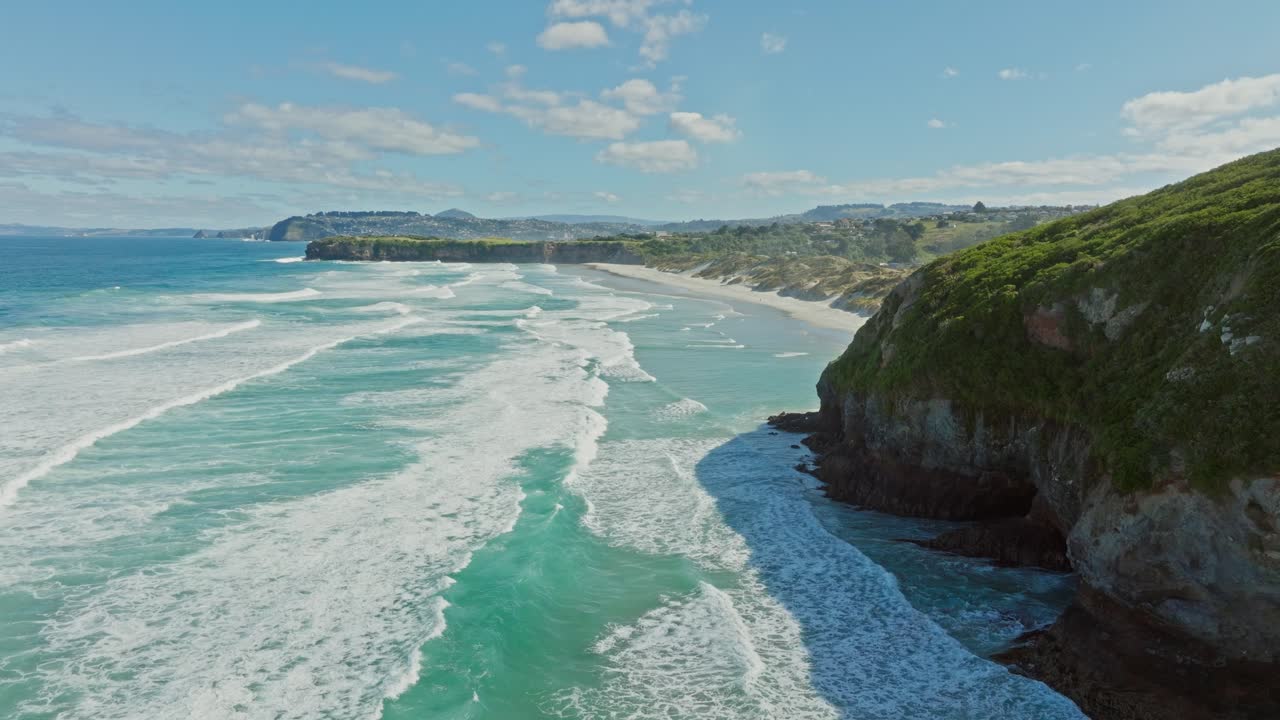 Scenic aerial view over ocean with rolling white wash waves, white sandy beach and sand dunes at Smails Beach on the Otago Peninsula, Dunedin, New Zealand Aotearoa