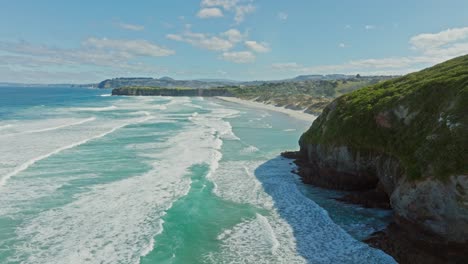 scenic aerial view over ocean with rolling white wash waves, white sandy beach and sand dunes at smails beach on the otago peninsula, dunedin, new zealand aotearoa