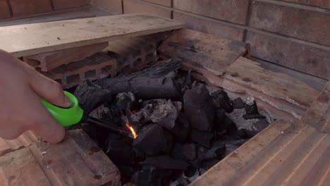 slow motion wide shot of man lighting a charcoal greek style bbq at dusk with a safety gas lighter